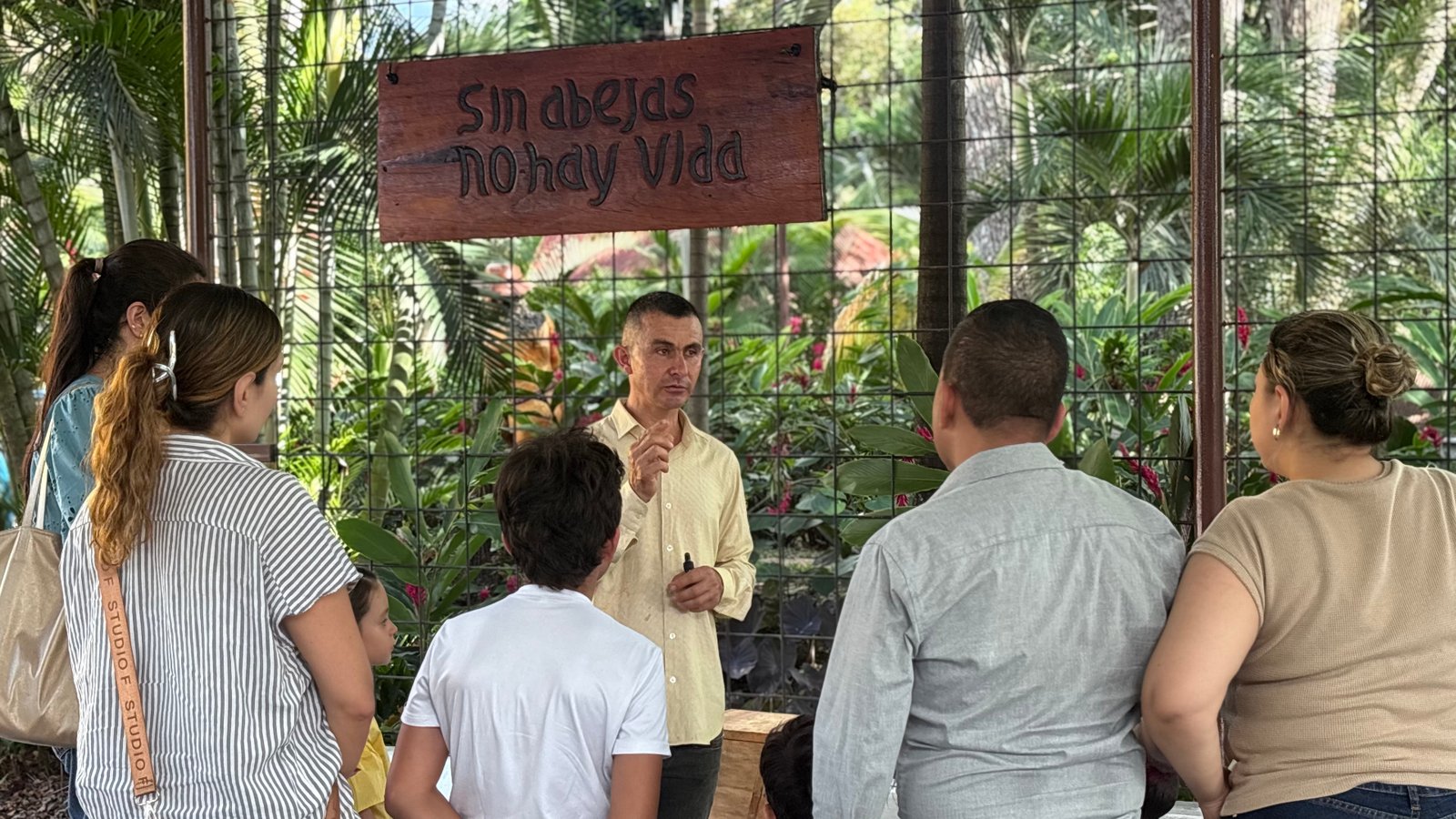 Guía experto explicando a familias en el museo vivo, bajo el letrero 'Sin abejas no hay vida'